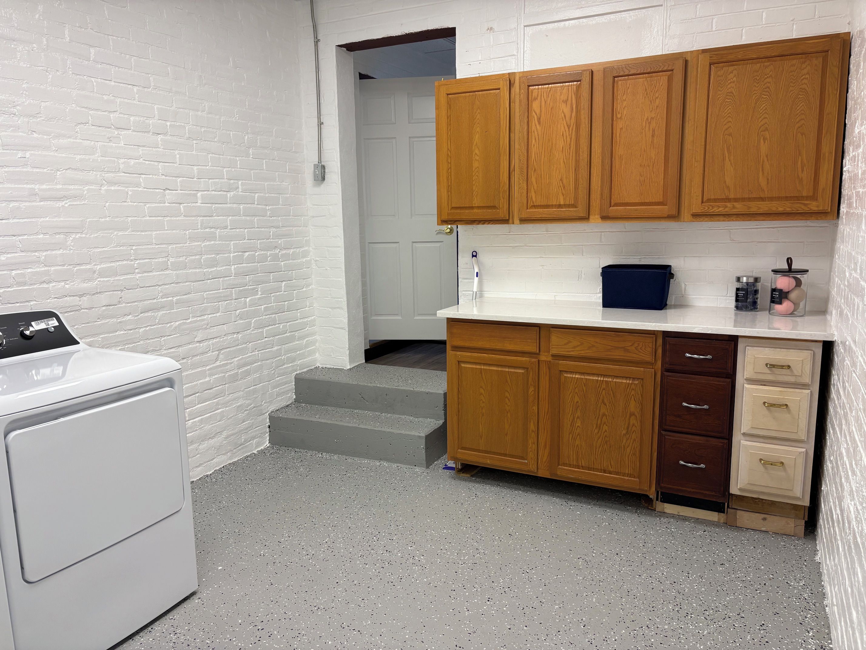 Un espace buanderie comprenant un lave-linge, des armoires en bois et un plan de travail avec des bocaux.