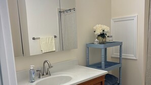 Ein Badezimmer mit einem weißen Waschbecken, Holzschränken, einem Spiegel und einem blauen Regal mit einer Blumenvase.