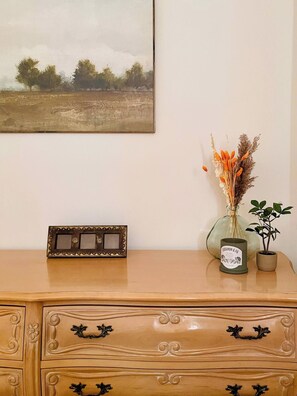 A wooden dresser with a framed picture above it, a vase with dried flowers, and a small potted plant. - The Corner Saloon with desert and mountain views (Twentynine Palms)