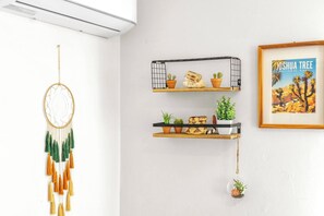 A room with a dreamcatcher, two shelves with plants and decorative items, and a framed picture of Joshua Tree National Park. - The Corner Saloon with desert and mountain views (Twentynine Palms)