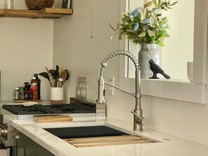 A kitchen with a stainless steel range, a modern faucet, and a window sill with a vase of flowers. - The Corner Saloon with desert and mountain views (Twentynine Palms)