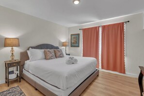A hotel room with a bed, bedside tables, a lamp, a picture on the wall, and a window with curtains. - The Corner Saloon with desert and mountain views (Twentynine Palms)