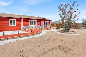A red building with a stone foundation, a paved driveway, and a desert landscape. - The Corner Saloon with desert and mountain views (Twentynine Palms)