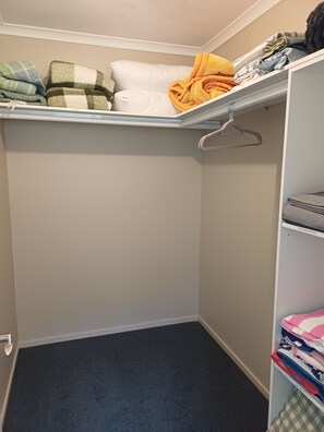 Ein Kleiderschrank mit Regalen und Kleiderbügeln, gefüllt mit zusammengefaltetem Wäsche und Decken.