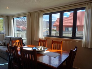 Ein Essbereich mit Holztisch und Stühlen, einer Couch und großen Fenstern mit Vorhängen.