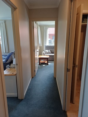 Ein Flur mit Teppichboden, der in einen Wohnbereich mit einer Couch und einem kleinen Tisch führt.