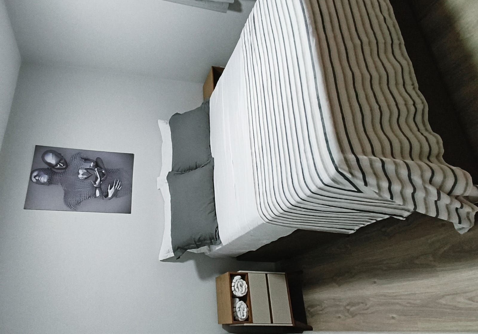 A bedroom with a bed, a nightstand, and a wall-mounted artwork.