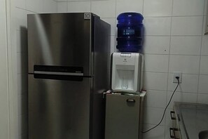 Un refrigerador de acero inoxidable con dispensador de agua en la parte superior, un pequeño congelador y un enchufe de pared.
