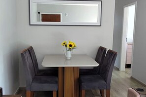 Een eethoek met een tafel en stoelen, een vaas met bloemen en een spiegel aan de muur.
