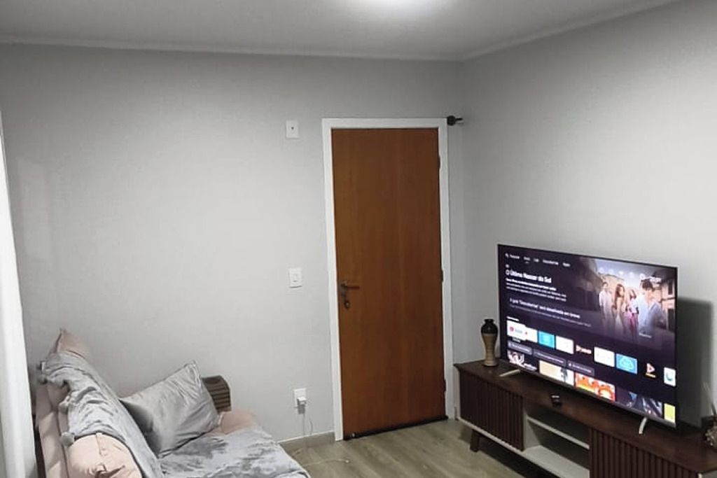 Una habitación con cama, televisor en un mueble, una puerta y un enchufe.