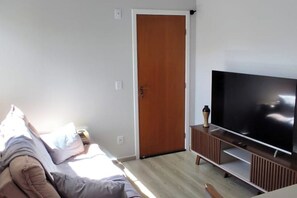 Een kamer met een bed, een televisie op een houten standaard en een deur.