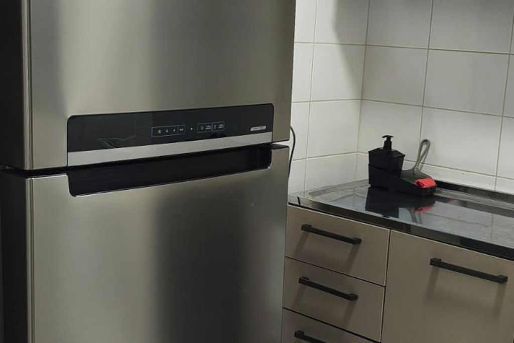 A stainless steel refrigerator with a digital control panel, a black countertop, and a red soap dispenser.