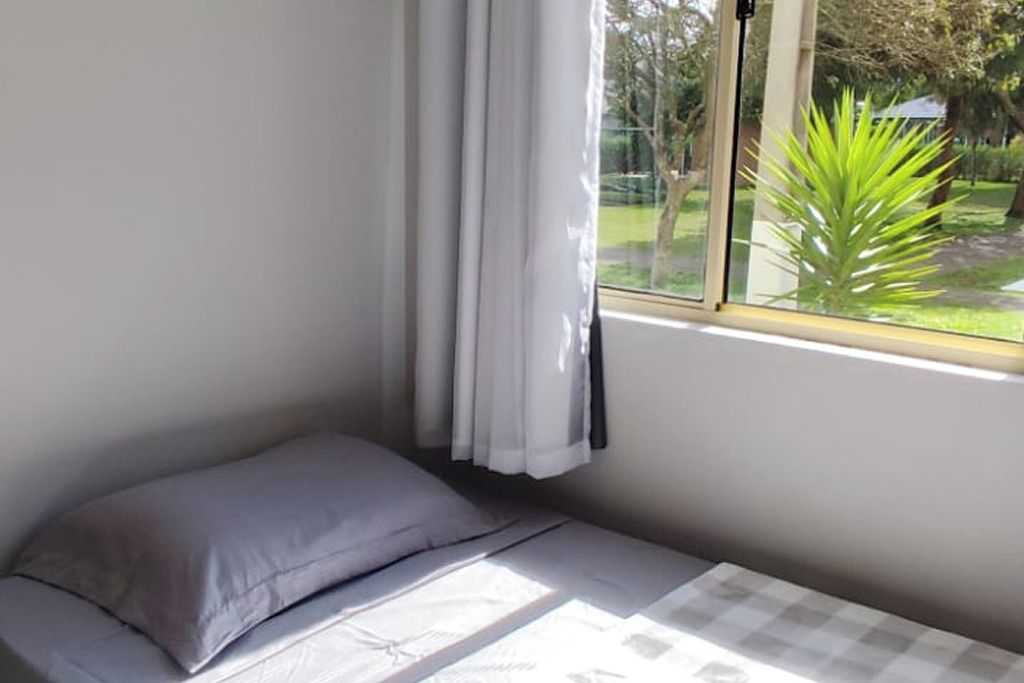 Ein Zimmer mit einem Bett, einem Vorhangfenster und Blick auf Grün.