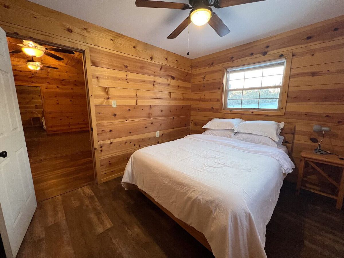 Una habitación con paneles de madera, una cama, un ventanal y un ventilador de techo.