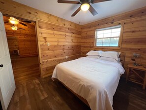 A wooden-paneled room with a bed, a window, and a ceiling fan.