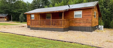 A wooden cabin with a porch, a metal roof, and a gravel driveway.