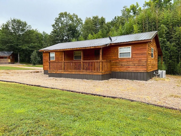 A wooden cabin with a porch, a metal roof, and a gravel driveway.