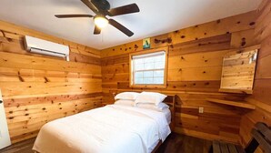 Quarto com cama, ventoinha no teto, janela e paredes de madeira.