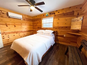 Une pièce avec un lit, un ventilateur de plafond, une fenêtre et des murs en bois.