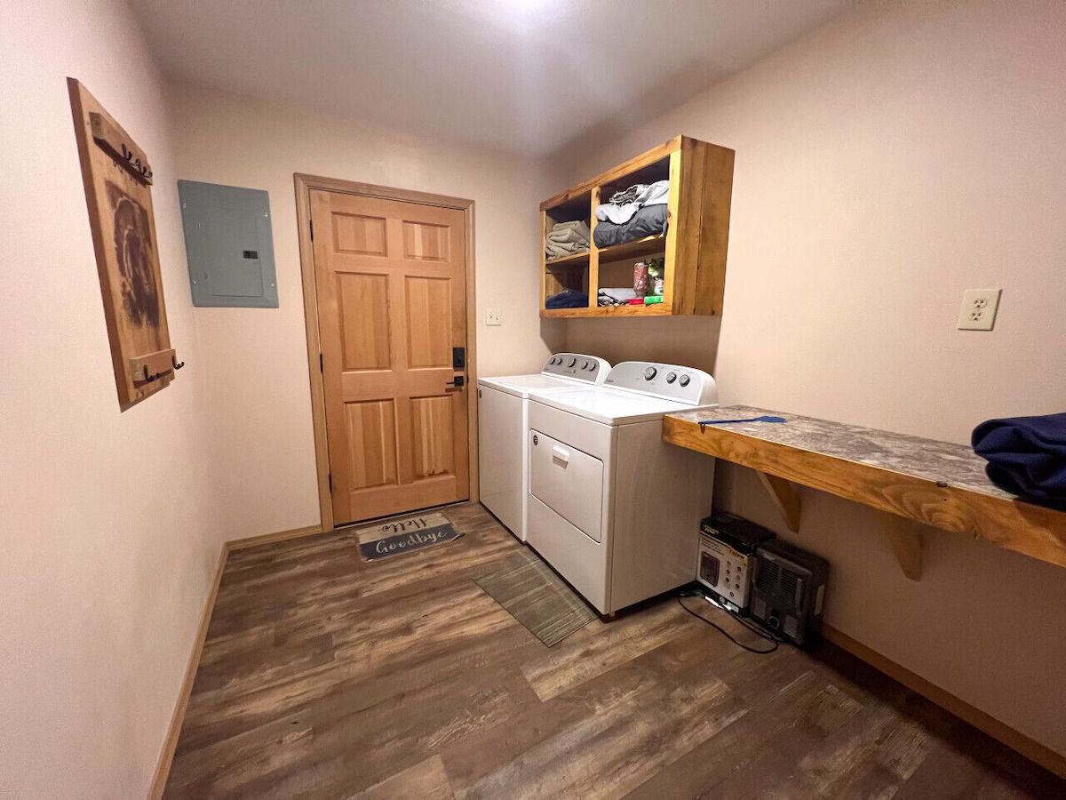 A laundry room with a washing machine, dryer, and wooden shelving unit.