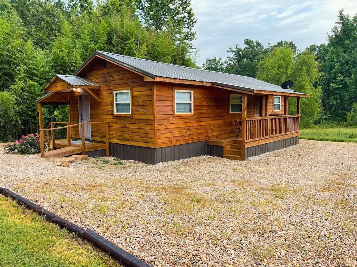 A wooden cabin with a porch, a satellite dish, and a gravel driveway.