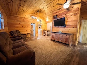 L'intérieur d'une cabane en rondins, avec un canapé, un téléviseur et un coin cuisine.