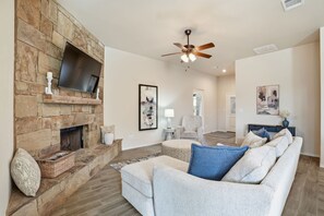 Ein Wohnzimmer mit Kamin aus Stein, einem darüber angebrachten Flachbildfernseher, einem Deckenventilator und einer Couch mit vielen Kissen.