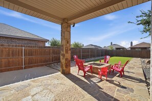 A covered patio area with stone flooring, red chairs, and a fire pit. - Stone and Sage - 3BR/2BA - Quiet Family Retreat (Lubbock)