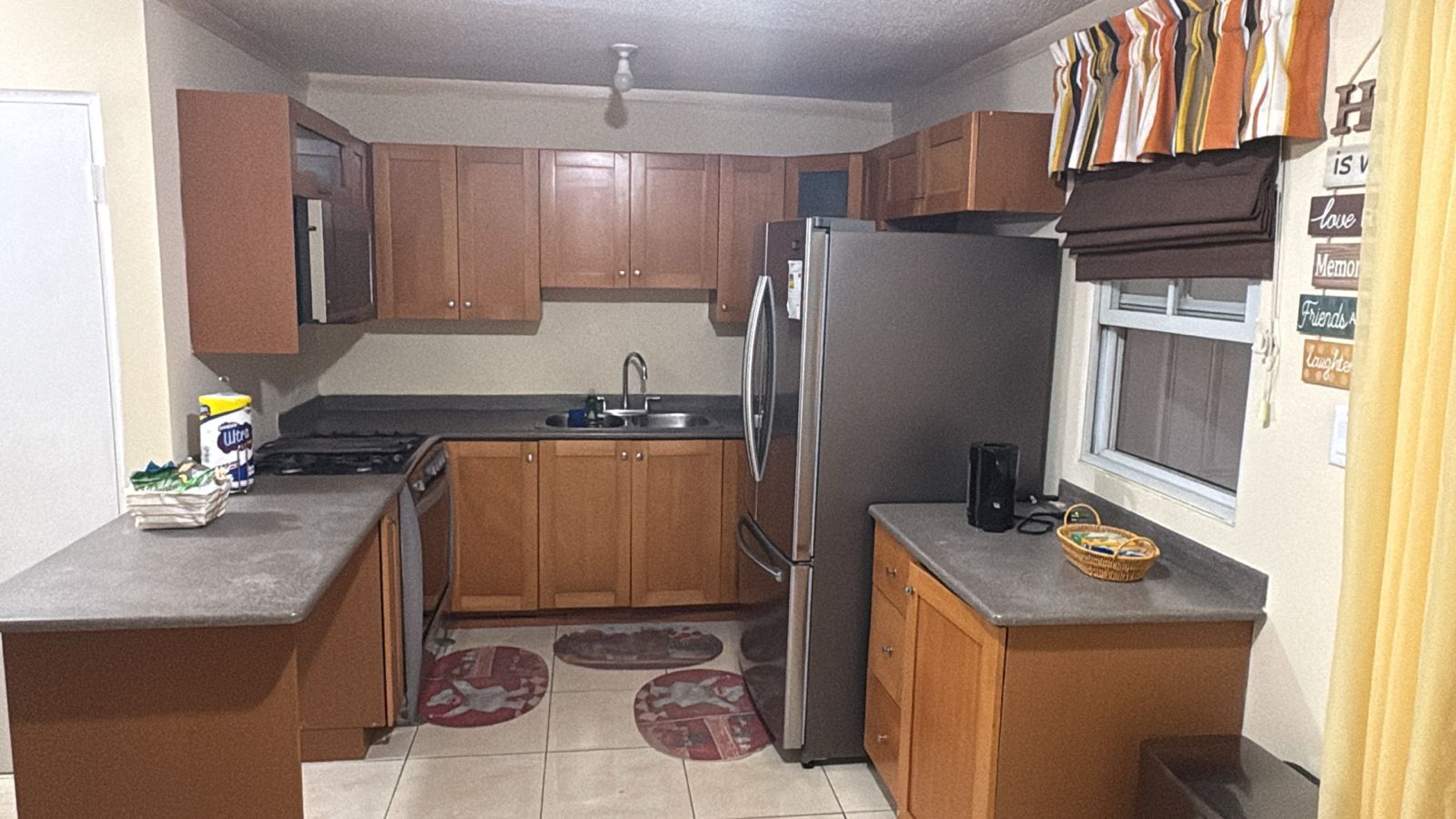 A compact kitchen with wooden cabinets, a stainless steel refrigerator, a sink, and a window.