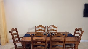 A dining table with six wooden chairs, a blue table runner, and a wall-mounted television. - Jacar Purple Blossom a cozy 2-bedroom townhome (Spanish Town)