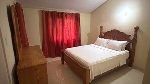A bedroom with a wooden bed, a wooden nightstand, and a red curtain. - Jacar Purple Blossom a cozy 2-bedroom townhome (Spanish Town)