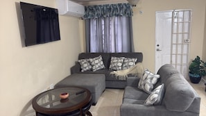 A living room with a grey sofa, a glass coffee table, and a white door. - Jacar Purple Blossom a cozy 2-bedroom townhome (Spanish Town)