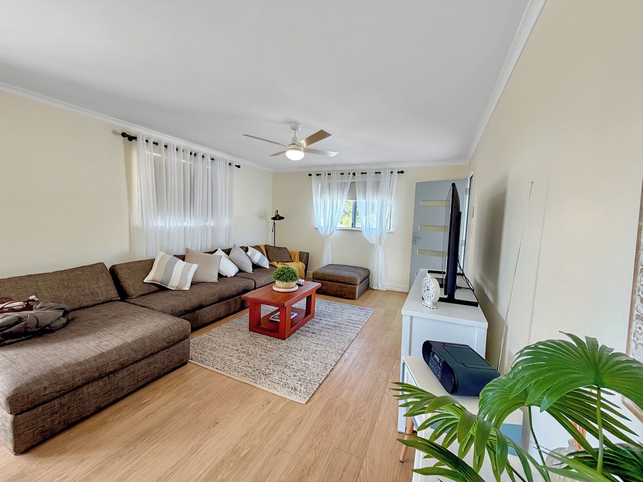 A living room with a sectional sofa, a coffee table, a television, and a ceiling fan.