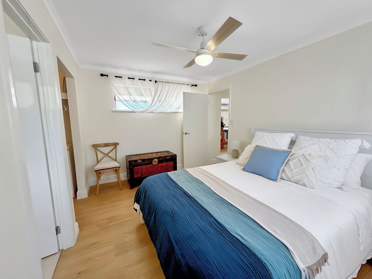 A bedroom with a bed, a ceiling fan, a window with curtains, a wooden chest, and a chair.