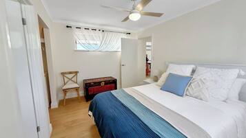 A bedroom with a bed, a ceiling fan, a window with curtains, a wooden chest, and a chair.