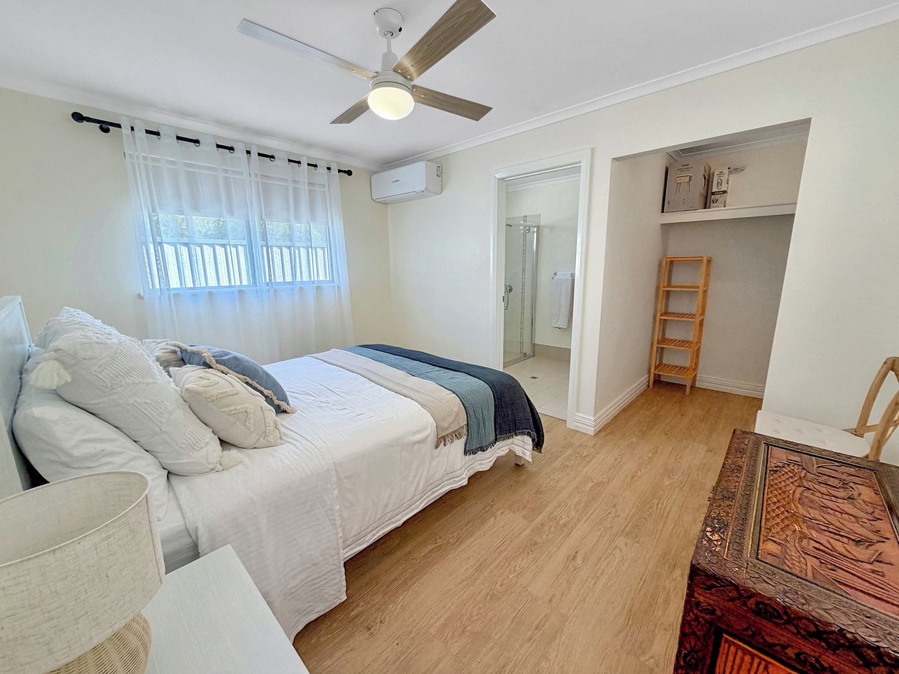 Un dormitorio con cama, ventilador de techo, ventana con cortinas y suelo de madera.