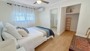 Un dormitorio con cama, ventilador de techo, ventana con cortinas y suelo de madera.