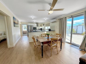 Uma ampla área de refeições com mesa e cadeiras de madeira, ventilador de teto e vista para área externa por uma porta de vidro deslizante.