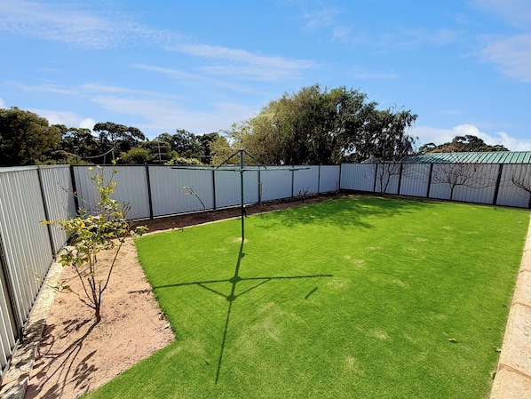 A fenced backyard with artificial grass, a small tree, and a metal fence. - Preston Beach Retreat (Preston Beach)