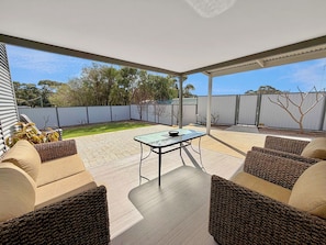 Um pátio externo com mesa e cadeiras, cercado por móveis de vime.