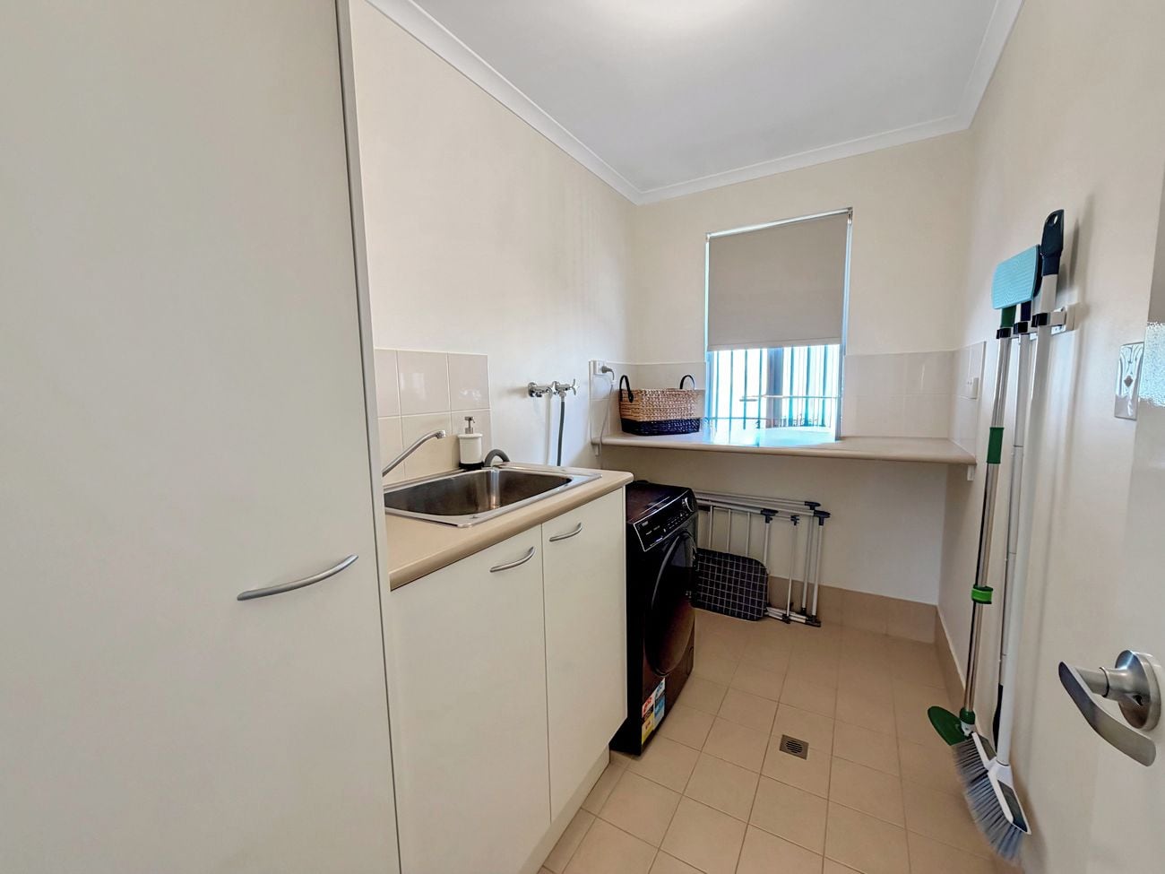 A compact kitchen with a sink, a washing machine, and a window with blinds.