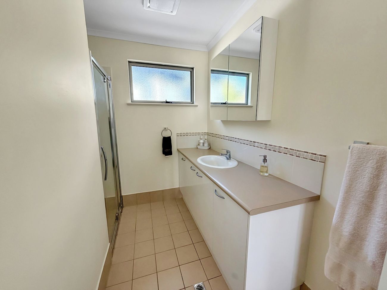 A bathroom with a shower, a sink, a mirror, and a towel rack.