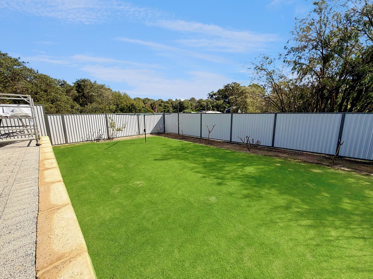 A fenced outdoor area with artificial green turf, a gravel path, and a metal fence.