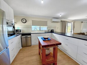 Una cocina moderna con armarios blancos, electrodomésticos de acero inoxidable, una mesa de madera y un reloj en la pared.