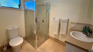 Un baño con ducha de vidrio, inodoro, lavamanos y dos toallas colgadas en un perchero.