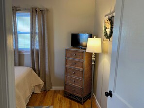 A bedroom with a bed, a television on a dresser, a lamp, and a door with a wreath decoration. - Cute and Cozy 3 Bedroom House in Saint Albans (Saint Albans)