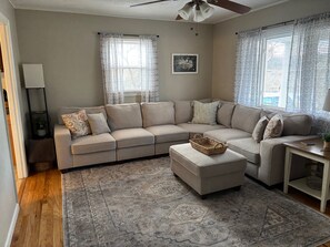 A living room with a beige sectional sofa, a patterned rug, and a ceiling fan. - Cute and Cozy 3 Bedroom House in Saint Albans (Saint Albans)