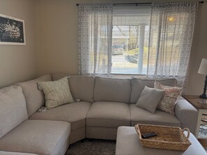 Ein beiges Modulsofa mit Fernbedienung auf einem Beistelltisch, einem gemusterten Zierkissen und einem gerahmten Bild an der Wand.