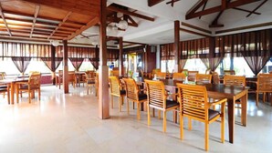 A spacious dining area with wooden tables and chairs, large windows with curtains, and a high ceiling with exposed beams. - Dago Highland Resort (Bandung)
