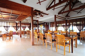 A spacious dining area with wooden tables and chairs, large windows with curtains, and a high ceiling with exposed beams. - Dago Highland Resort (Bandung)